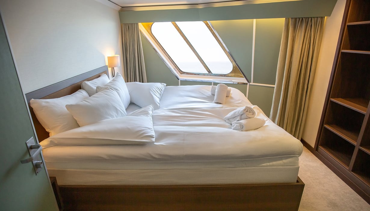 Cabin with a neatly made bed, window, and towel swans.