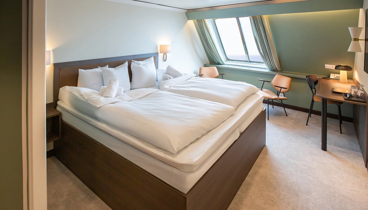 Modern cabin on the ship with a large bed, two chairs, and a desk.