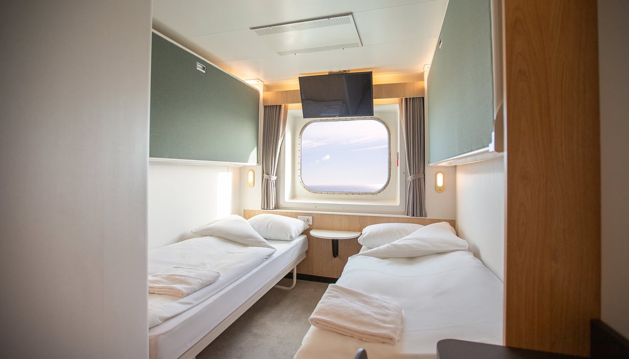 Cabin with two single beds, window, and ceiling-mounted TV.