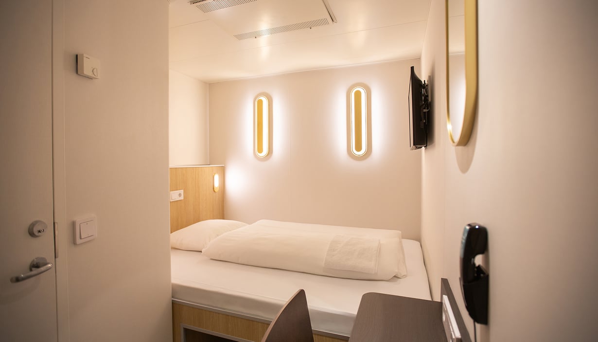 Modern cabin with a single bed, wall-mounted lights, and TV.