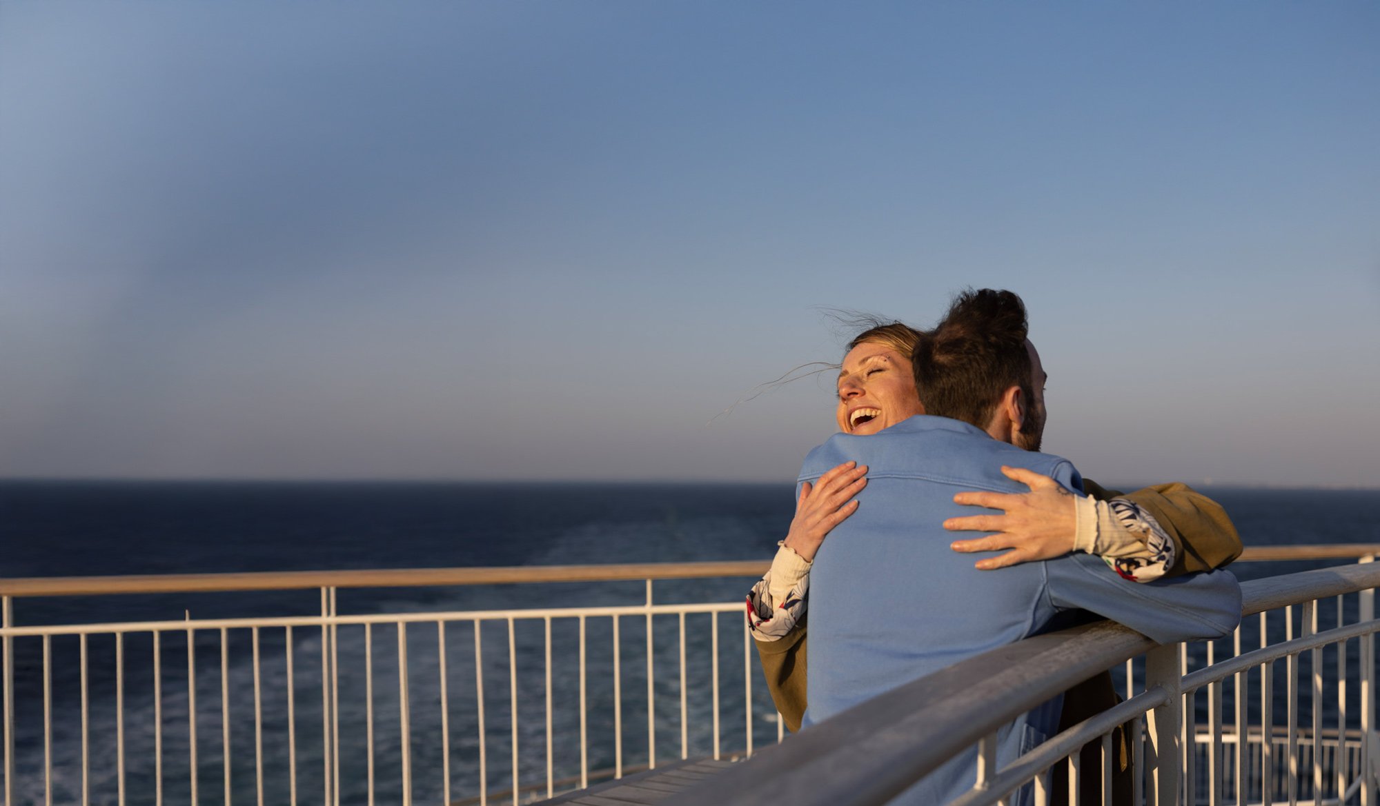 Two people embracing on a balcony overlooking the sea.