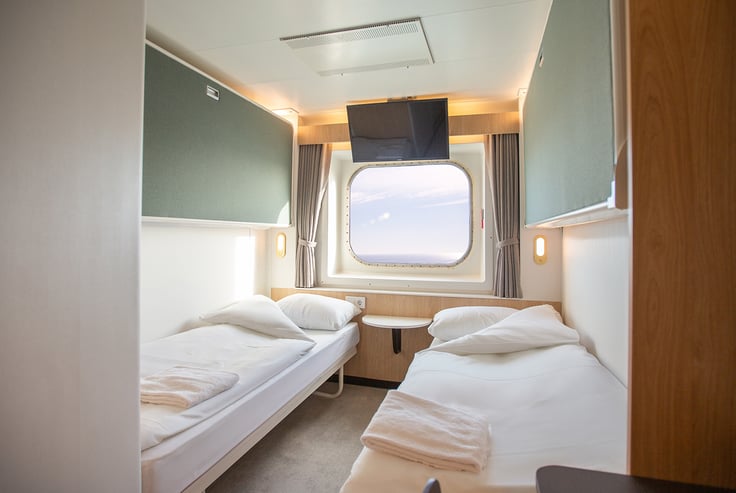 Cabin with two single beds, window, and ceiling-mounted TV.