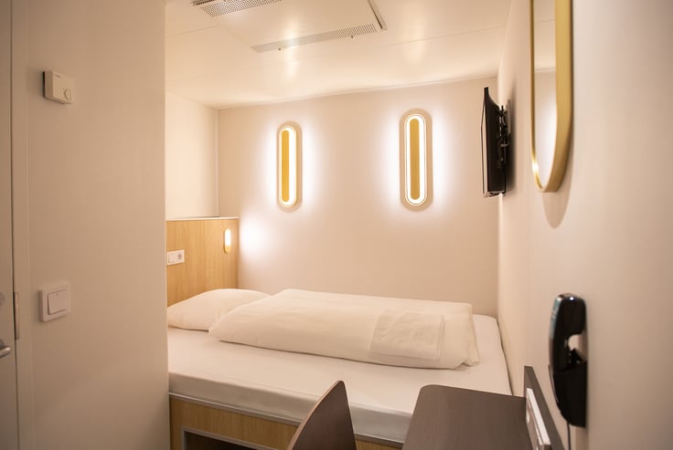 Modern cabin with a single bed, wall-mounted lights, and TV.