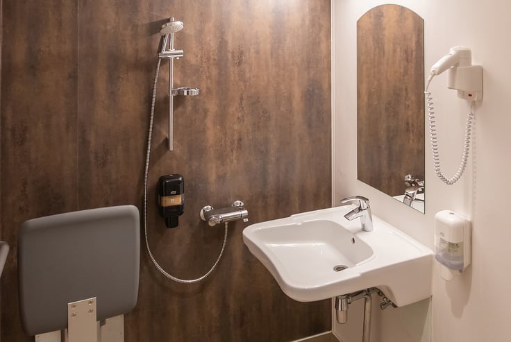 Accessible bathroom with sink, shower, and foldable seat.