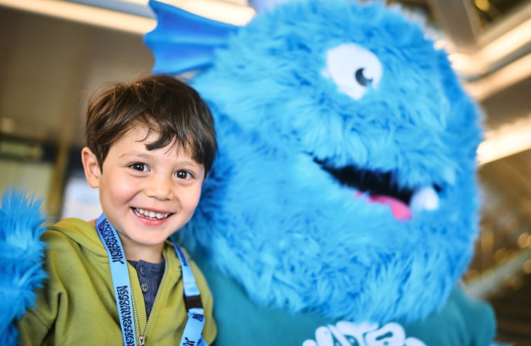 Person standing next to a large blue furry mascot with white eyes and a big smile in the Matrosklubben.